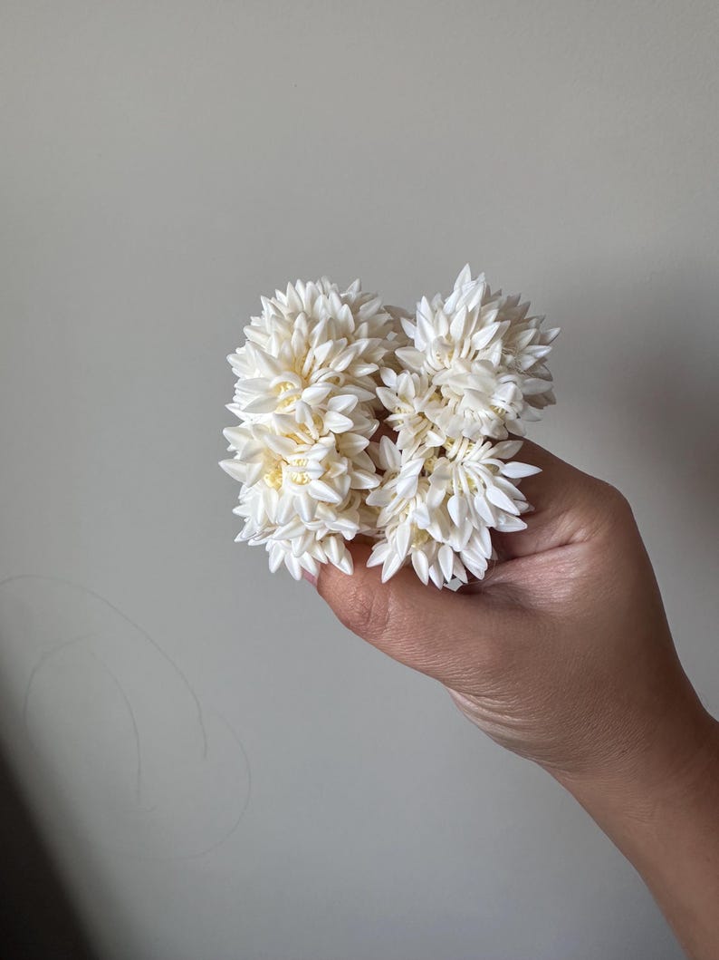 K&ouml;nnte beinhalten: Zwei wei&szlig;e Blumenkr&auml;nze aus Stoff, die in einer Hand gehalten werden.