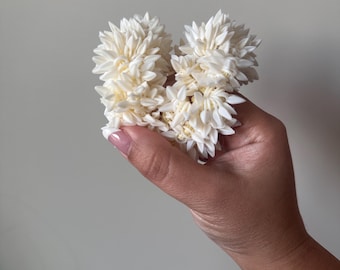 Può includere: Una ghirlanda di fiori bianchi fatta di piccoli fiori delicati. La ghirlanda è tenuta in una mano, con i fiori disposti a forma di cuore.