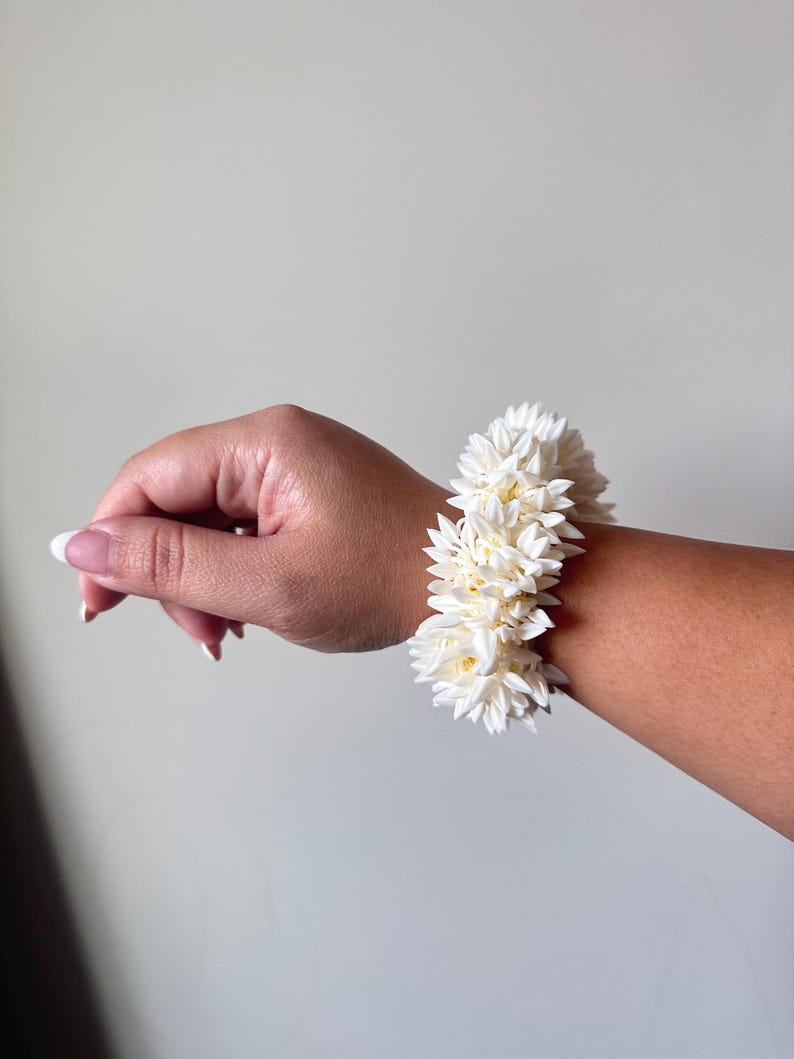 K&ouml;nnte beinhalten: Ein wei&szlig;es Blumenarmband aus kleinen, zarten Bl&uuml;ten. Das Armband wird am Handgelenk getragen.