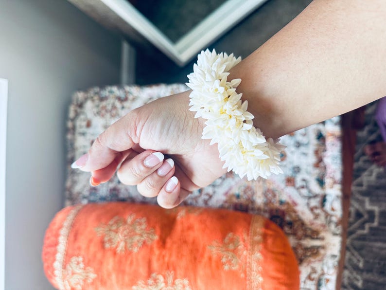 K&ouml;nnte beinhalten: Ein wei&szlig;es Blumenarmband aus kleinen wei&szlig;en Bl&uuml;ten. Das Armband wird am Handgelenk getragen.