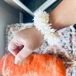 K&ouml;nnte beinhalten: Ein wei&szlig;es Blumenarmband aus Jasminbl&uuml;ten. Das Armband wird am Handgelenk getragen.