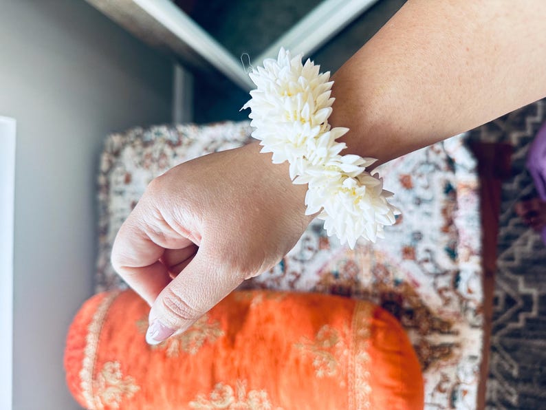 K&ouml;nnte beinhalten: Ein wei&szlig;es Blumenarmband aus Jasminbl&uuml;ten. Das Armband wird am Handgelenk getragen.