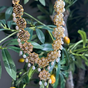 May include: A gold necklace with a floral design and pearl accents. The necklace is made of metal and has a delicate, intricate design.