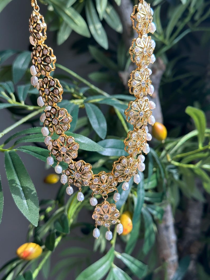 May include: A gold necklace with a floral design and pearl accents. The necklace is made of metal and has a delicate, intricate design.