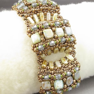 Könnte beinhalten: Ein mehrreihiges Perlenarmband mit geometrischem Muster. Das Armband besteht aus braunen, grünen und weißen Perlen. Das Armband liegt auf einem weißen Hintergrund.