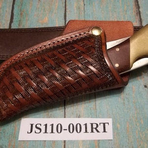 May include: A brown leather knife sheath with a woven pattern and a brass snap. The sheath is attached to a brown leather belt. The text "JS110-001RT" is printed on a white label.