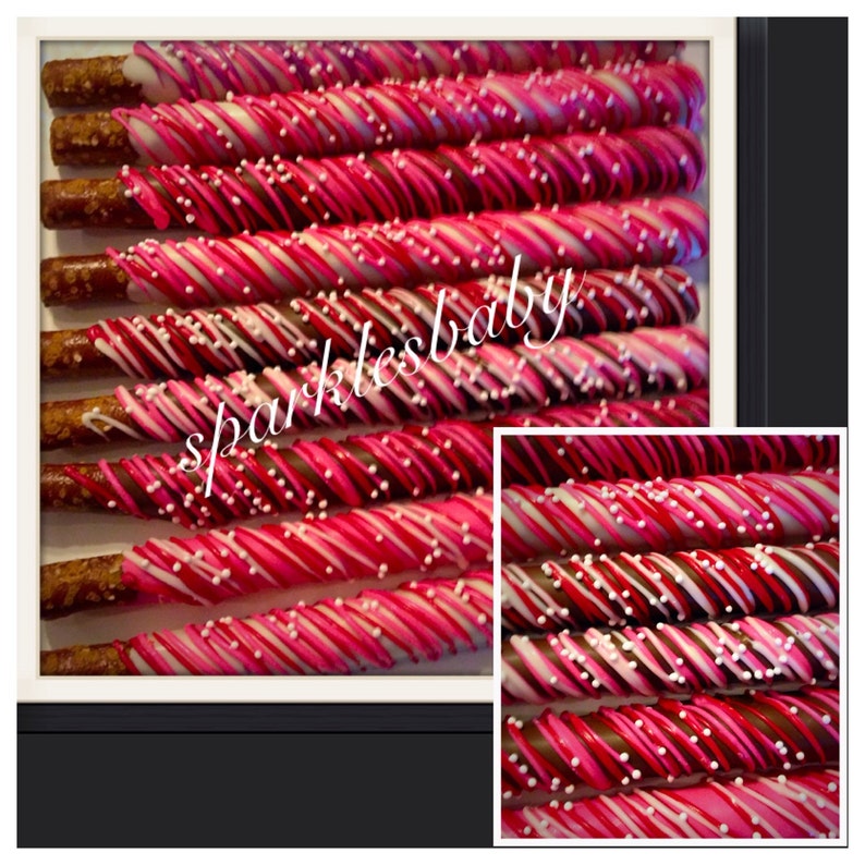 May include: Close-up of chocolate-covered pretzel rods with pink, white, and dark chocolate stripes, and white sprinkles. The image includes the text "sparklesbaby". These treats are arranged in rows, perfect for a sweet snack or gift.