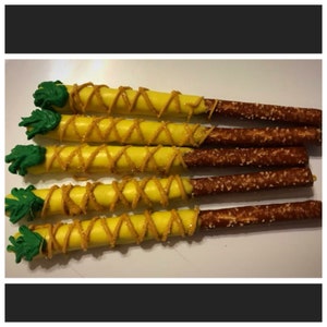 May include: A close-up of six pretzel rods dipped in yellow chocolate and decorated with green frosting to resemble pineapples.