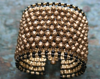 May include: A gold and black beaded bracelet with a geometric pattern. The bracelet is made of small, round beads that are woven together to create a unique and stylish design.