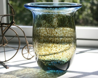 May include: A blue glass vase with a speckled brown and gold design. The vase is sitting on a white surface.