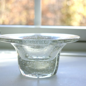 May include: A clear glass bowl with a wide, flat rim and a rounded base. The bowl is filled with small air bubbles, giving it a textured appearance.