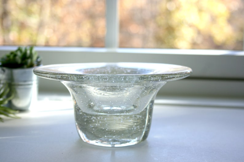 May include: A clear glass bowl with a wide, flat rim and a rounded base. The bowl is filled with small air bubbles, giving it a textured appearance.