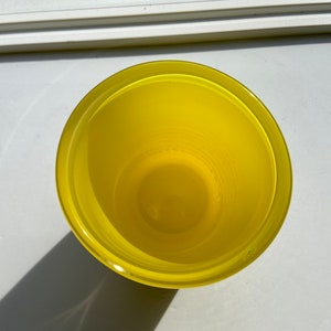 May include: A yellow glass cup with a smooth, rounded rim. The cup is empty and appears to be made of a clear glass.