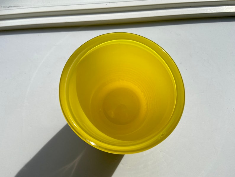 May include: A yellow glass cup with a smooth, rounded rim. The cup is empty and appears to be made of a clear glass.