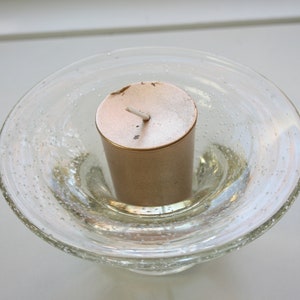 May include: A gold votive candle sits in a clear glass candle holder with a textured surface.