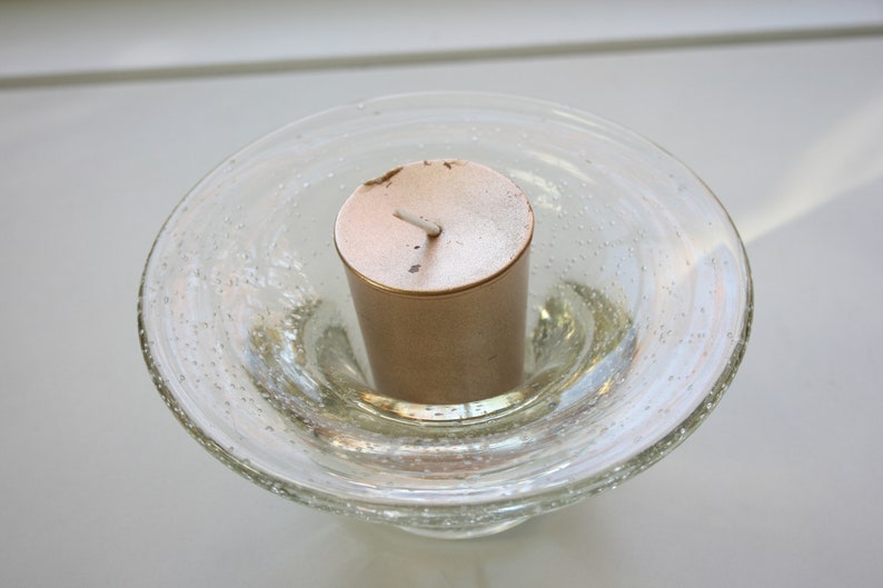 May include: A gold votive candle sits in a clear glass candle holder with a textured surface.