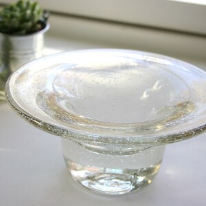 May include: A clear glass bowl with a wide, flat rim and a round base. The bowl has a textured surface with small air bubbles.
