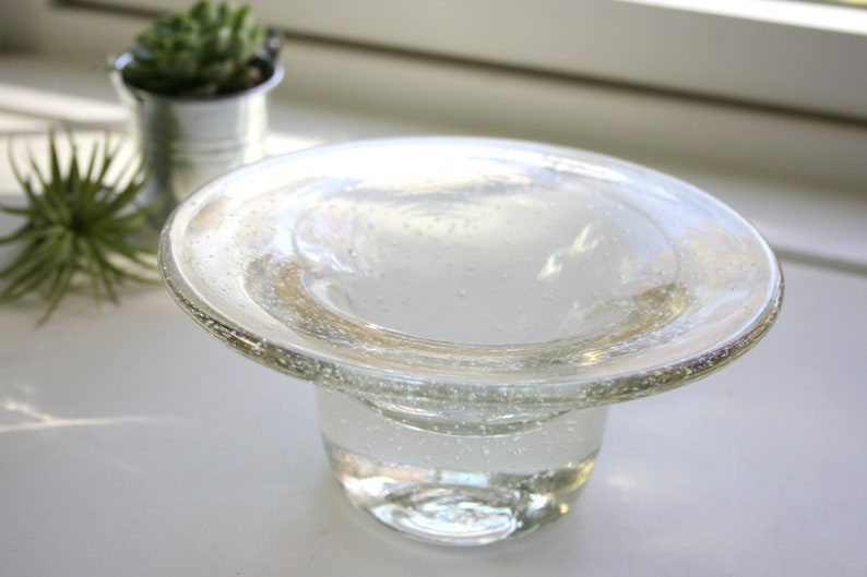 May include: A clear glass bowl with a wide, flat rim and a round base. The bowl has a textured surface with small air bubbles.