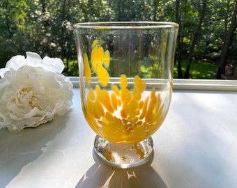 May include: A clear glass vase with a yellow speckled design. The vase has a round base and a wide mouth.