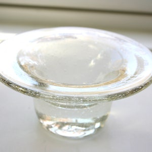 May include: A clear glass candle holder with a wide, flat top and a round base. The glass has a textured surface with small air bubbles.