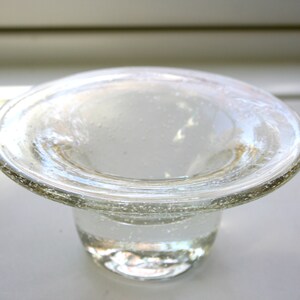 May include: A clear glass bowl with a wide, flat rim and a rounded base. The bowl has a textured surface and appears to be handmade.