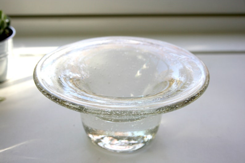 May include: A clear glass bowl with a wide, flat rim and a rounded base. The bowl has a textured surface and appears to be handmade.