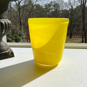 May include: A bright yellow glass vase with a rounded, slightly flared opening. The vase has a smooth, glossy finish and a subtle, rippled texture.