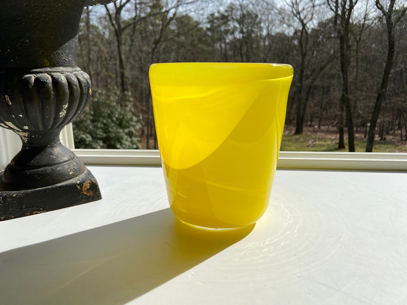May include: A bright yellow glass vase with a rounded, slightly flared opening. The vase has a smooth, glossy finish and a subtle, rippled texture.