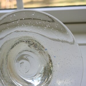 May include: A clear glass bowl with a textured surface. The bowl has a circular shape and a wide rim. The bowl is filled with small air bubbles.