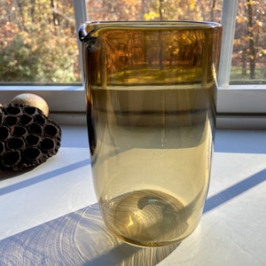 Puede incluir: Una jarra de vidrio transparente con un efecto degradado marrón. La jarra tiene una boca ancha y un asa.