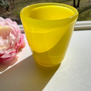 May include: A bright yellow glass vase with a rounded shape and a smooth, glossy finish.