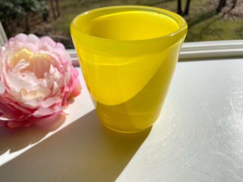 May include: A bright yellow glass vase with a rounded shape and a smooth, glossy finish.