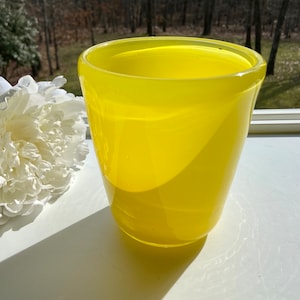 May include: A bright yellow glass vase with a rounded shape. The vase is sitting on a white surface.