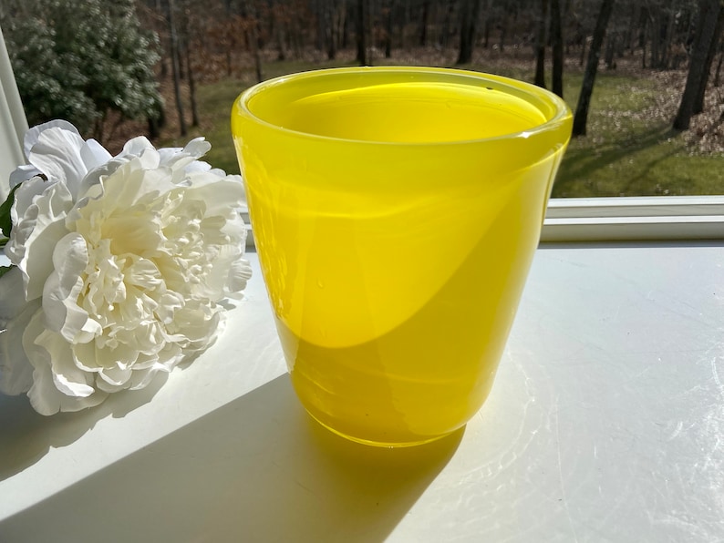 May include: A bright yellow glass vase with a rounded shape. The vase is sitting on a white surface.