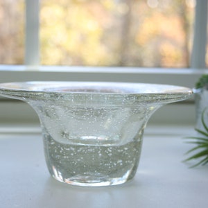 May include: A clear glass bowl with a wide, flared rim and a textured, bubbly surface. The bowl is sitting on a white surface.
