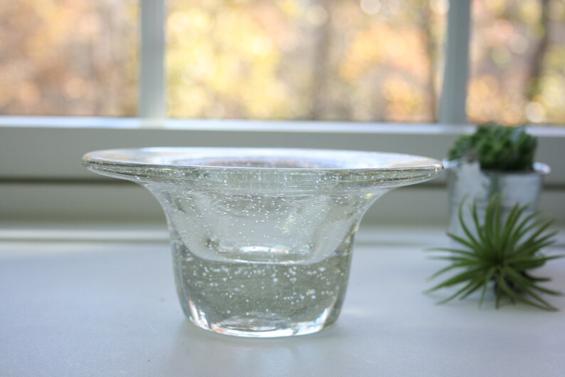 May include: A clear glass bowl with a wide, flared rim and a textured, bubbly surface. The bowl is sitting on a white surface.