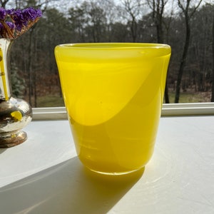 May include: A bright yellow glass vase with a rounded bottom and a slightly flared top.