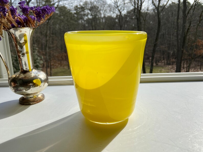 May include: A bright yellow glass vase with a rounded bottom and a slightly flared top.