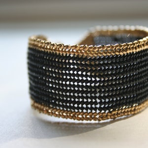 May include: A black and gold woven bracelet with a chain-like design.