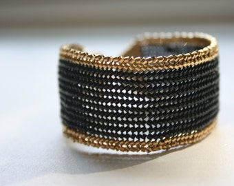 May include: A black and gold woven bracelet with a chain-like design.