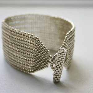 May include: A silver bracelet with a woven design and a toggle clasp.