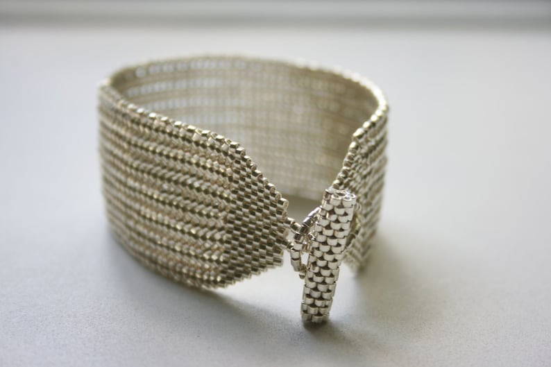 May include: A silver bracelet with a woven design and a toggle clasp.