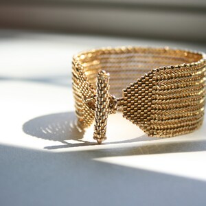 May include: A gold-toned bracelet with a woven design and a simple, straight clasp.