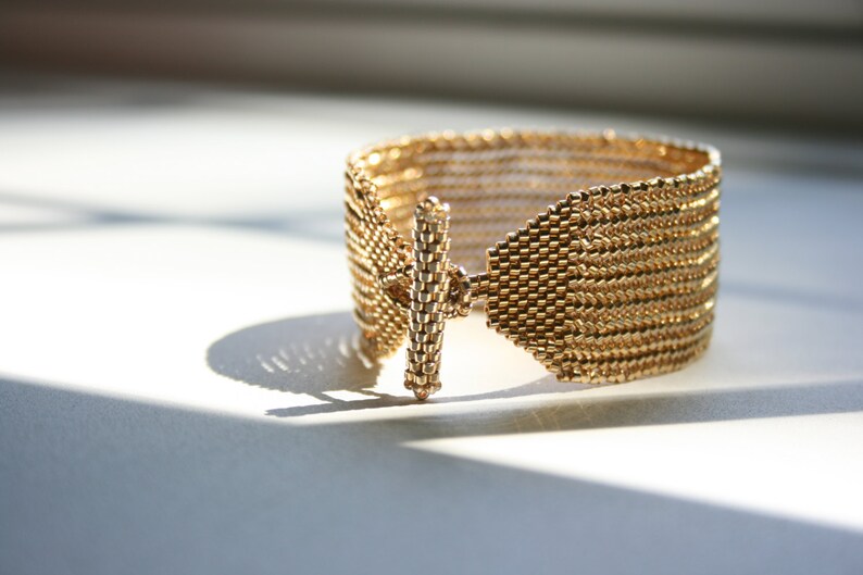 May include: A gold-toned bracelet with a woven design and a simple, straight clasp.