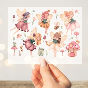 Può includere: Illustrazione ad acquerello con fate, funghi, fiori e una rana. Le fate sono raffigurate con abiti e ali a forma di fiore, nelle tonalità del rosa, giallo e verde. L'opera d'arte ha un'estetica stravagante da libro di fiabe.