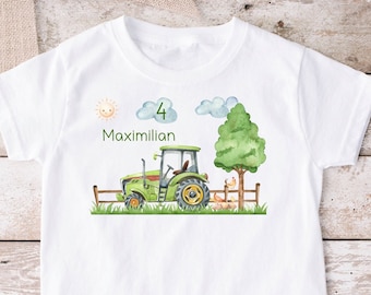 May include: White t-shirt with a green tractor, a tree, a sun, and clouds. The text "Maximillian 4" is printed on the shirt.
