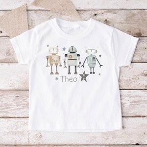 Könnte beinhalten: Weißes T-Shirt mit einem Aufdruck von drei Robotern und dem Namen "Theo" auf der Vorderseite.