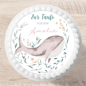 Könnte beinhalten: Ein runder Kuchen mit weißem Zuckerguss und einem dekorativen Rand. Der Kuchen zeigt eine Aquarellillustration eines Wals, umgeben von floralen Elementen. Der Text "Zur Taufe", das Datum und ein Name sind ebenfalls sichtbar.