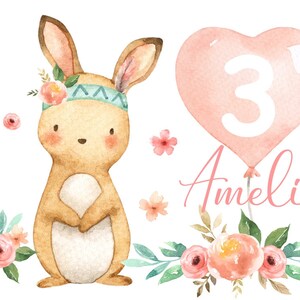 Könnte beinhalten: Eine Aquarell-Illustration eines niedlichen Kaninchens, das ein Stirnband mit Blumen und ein türkisfarbenes Perlen-Stirnband trägt. Das Kaninchen hält seine Pfoten zusammen und steht vor einem rosafarbenen herzförmigen Ballon mit der Zahl 3 darin. Der Ballon ist mit einer Schnur gebunden und der Name "Amelie" ist darunter geschrieben. Die Illustration ist von rosa und weißen Blumen und grünen Blättern umgeben.