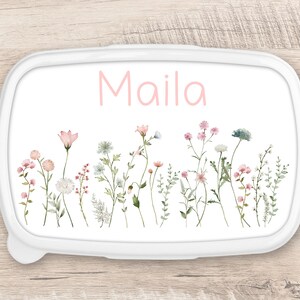 Peut inclure: Boîte à lunch blanche avec un motif floral rose et le nom "Maila" écrit en lettres roses.